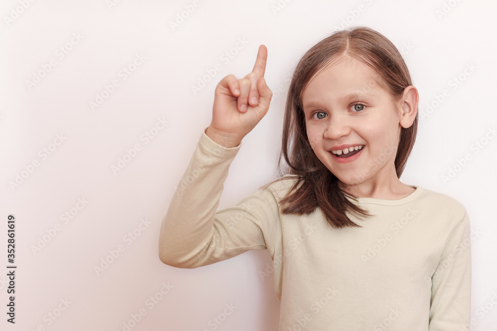 Little smiling girl in a light sweater on a light background raised her hand and shows her thumb up Little smiling girl in a light sweater on a light background raised her hand and shows her thumb up