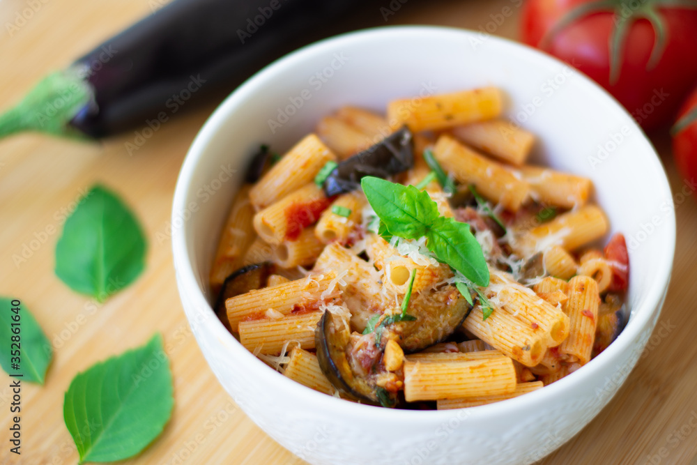 Traditional Italian dish: pasta alla norma with tomatoes, eggplant, garlic, basil and ricotta cheese on a wooden cutting board