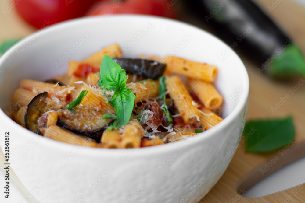 Traditional Italian dish: pasta alla norma with tomatoes, eggplant, garlic, basil and ricotta cheese on a wooden cutting board Traditional Italian dish: pasta alla norma with tomatoes, eggplant, garlic, basil and ricotta cheese on a wooden cutting board