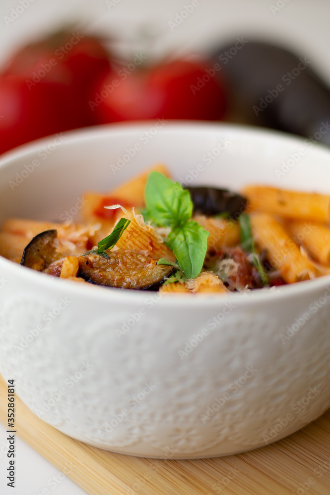 Traditional Italian dish: pasta alla norma with tomatoes, eggplant, garlic, basil and ricotta cheese on a wooden cutting board Traditional Italian dish: pasta alla norma with tomatoes, eggplant, garlic, basil and ricotta cheese on a wooden cutting board