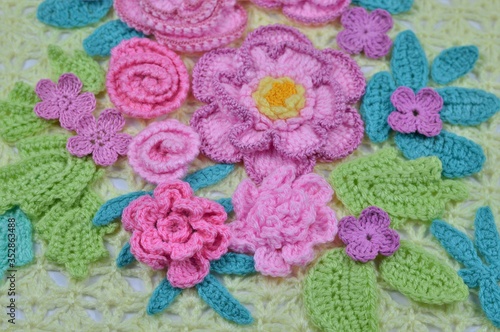 Colorful spring image from handmade crocheted flowers and leaves on a yellow lace background. 