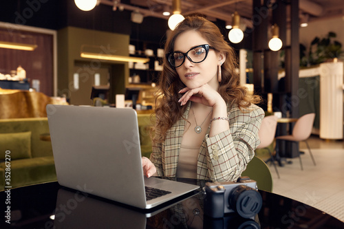 Confident young woman photographer in smart casual wear working on laptop