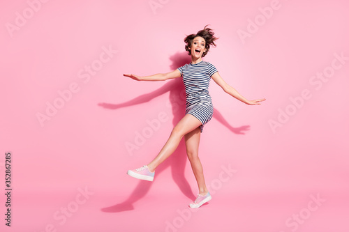 Full length photo of attractive lady skinny shapes good mood raise leg hands walking down street wear casual white blue striped dress shoes isolated pastel pink color background