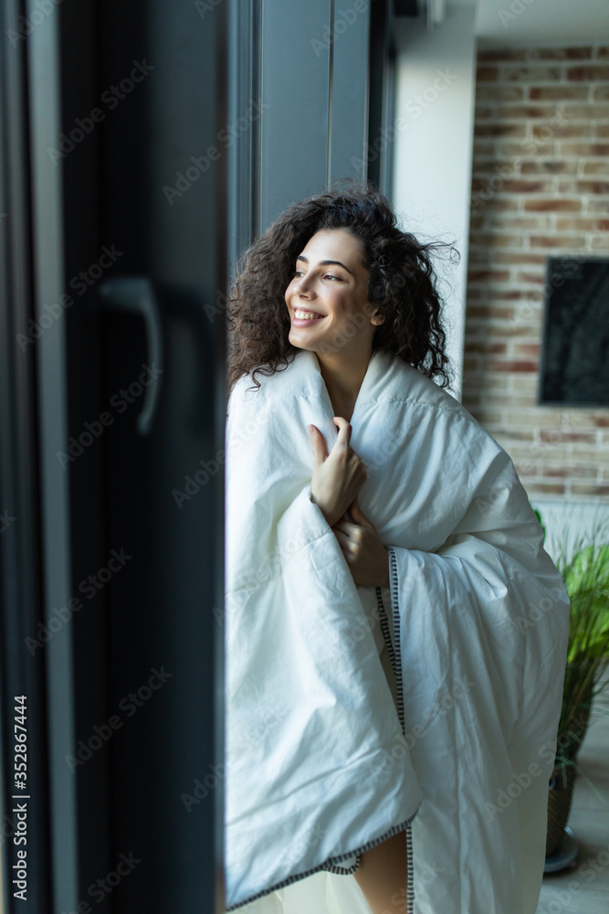 Beautiful woman standing in white blanket in light room, morning, relax time at home Beautiful woman standing in white blanket in light room, morning, relax time at home