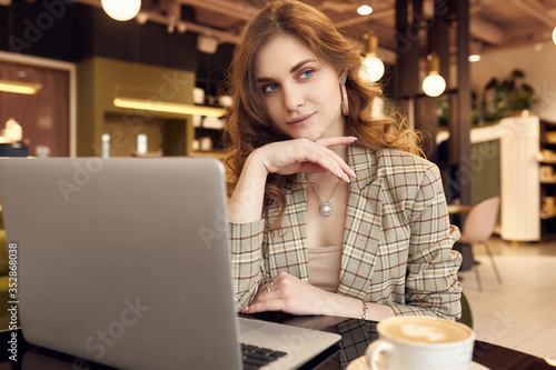 Young businesswoman in smart casual wear drinks coffee and working on laptop