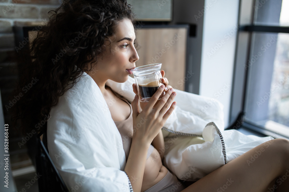 Young woman enjoying a cup of coffee sitting by a window in a sunny morning Young woman enjoying a cup of coffee sitting by a window in a sunny morning