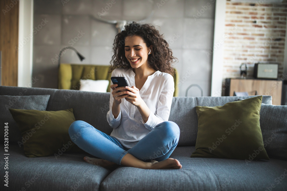 Happy young girl using her smartphone on the couch at home in the living room Happy young girl using her smartphone on the couch at home in the living room