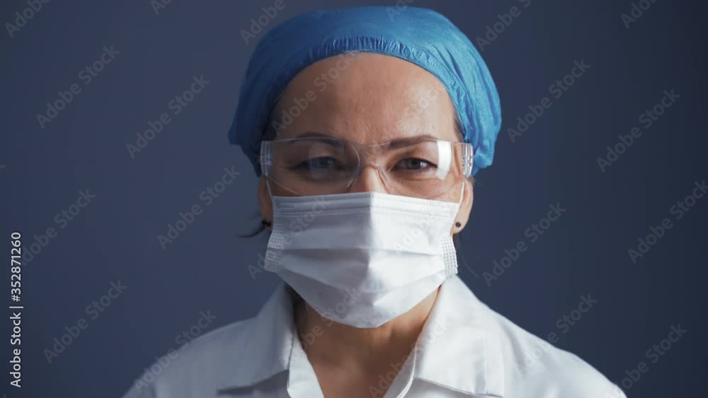 Camera zoom over doctor woman in protective mask and glasses wearing medical uniform isolated on dark blue background. Medicine concept. Prores 422 Camera zoom over doctor woman in protective mask and glasses wearing medical uniform isolated on dark blue background. Medicine concept. Prores 422