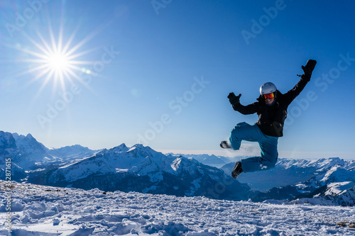 Girl with goggles and helmet is leaping midair in winter.