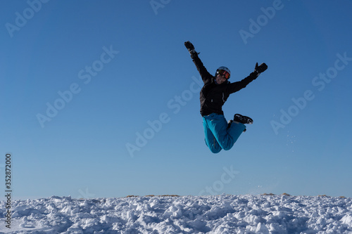 Girl with goggles and helmet is leaping midair in winter.