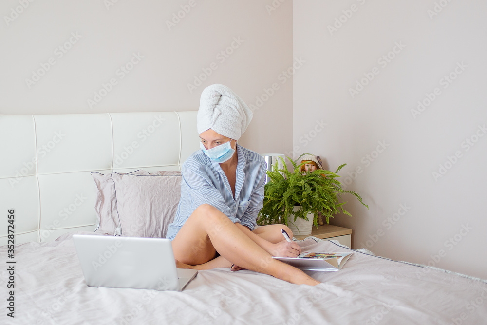 Woman in medical mask is working office work remotely from home on bed. Using computer. Distance learning online education and work Woman in medical mask is working office work remotely from home on bed. Using computer. Distance learning online education and work