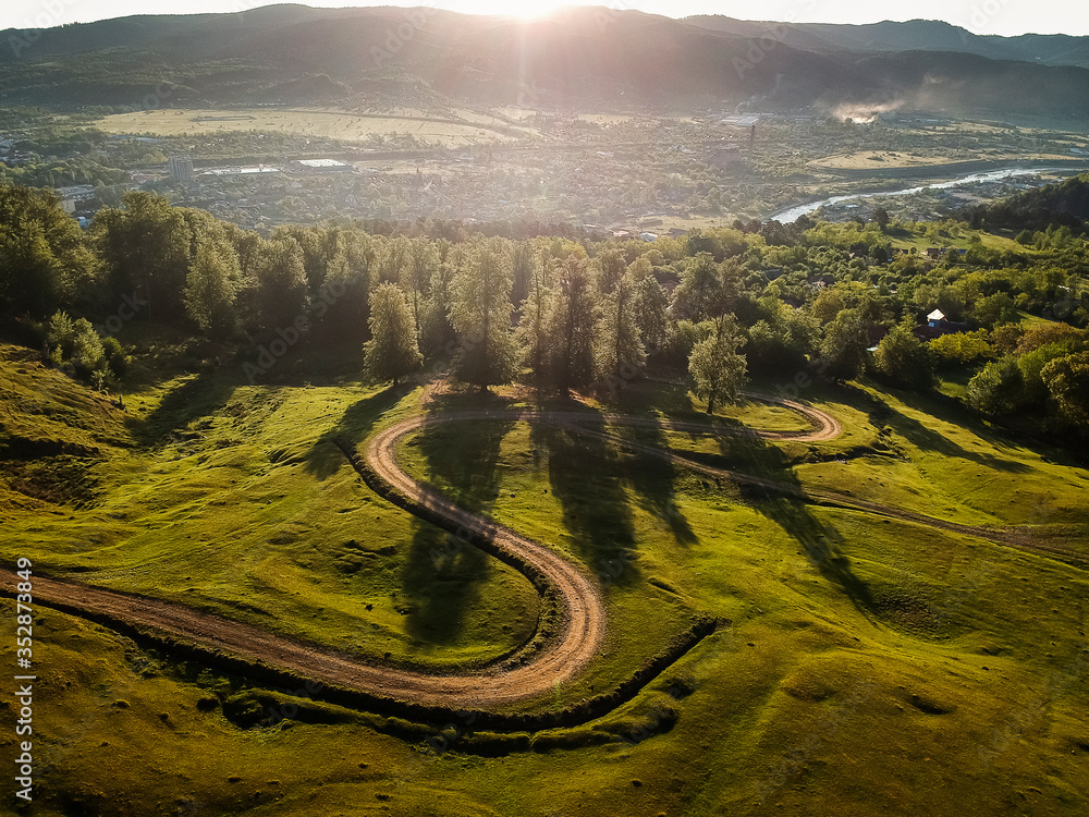 Beautiful curvy country road with fir trees in background during the sunrise with rays of light. Comanesti, Romania. Beautiful curvy country road with fir trees in background during the sunrise with rays of light. Comanesti, Romania.