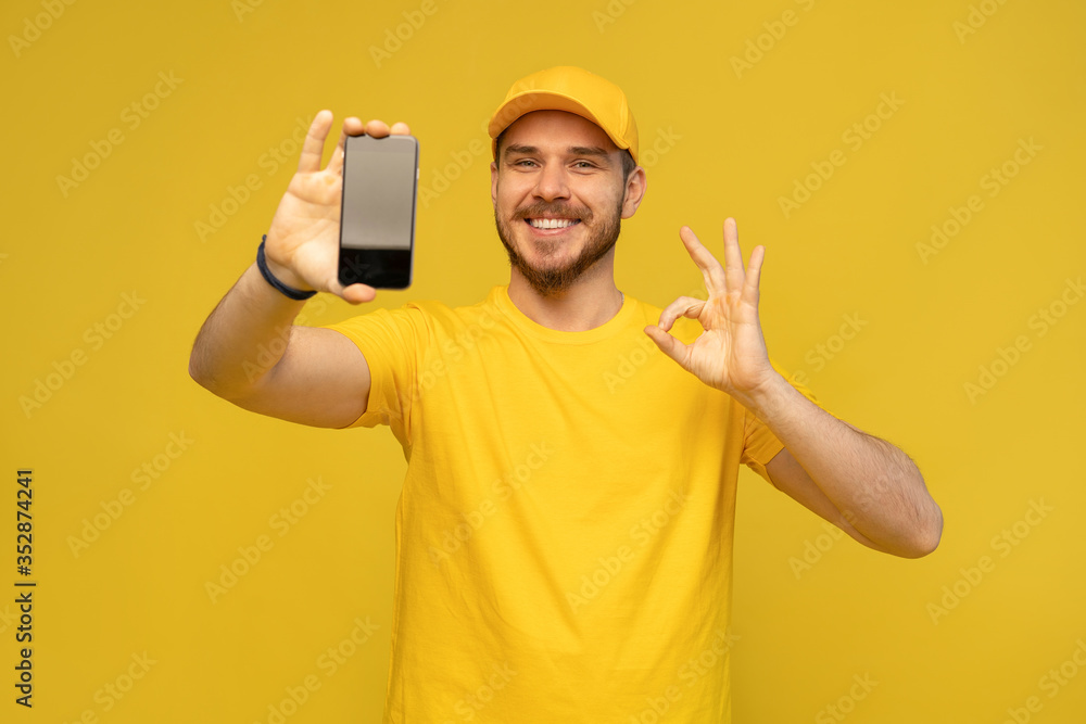 Portrait of a excited happy young delivery man in yellow cap standing isolated over white background