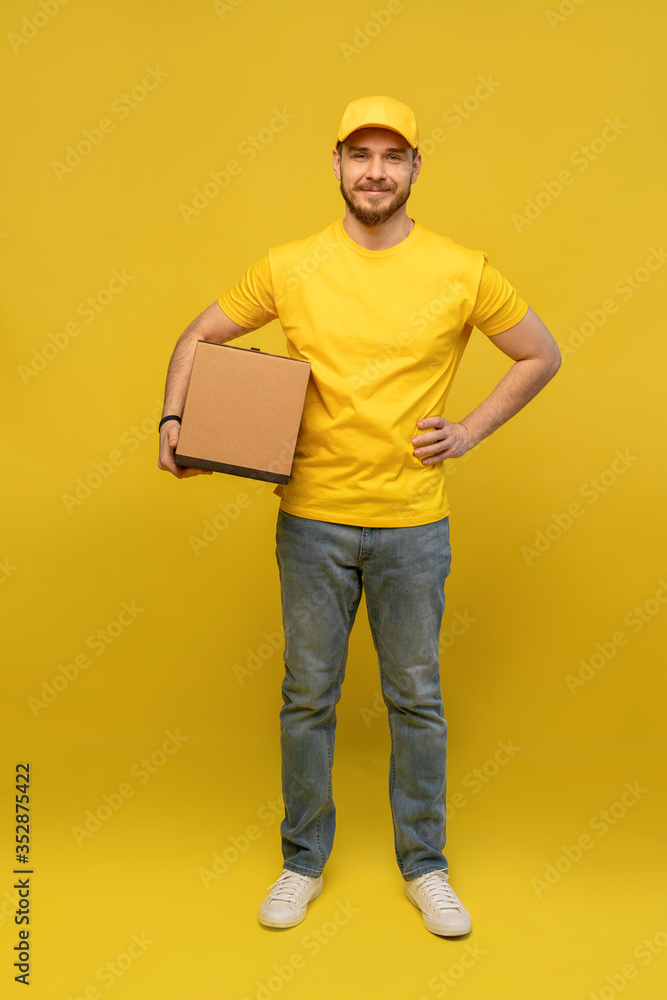 Portrait of excited delivery man in yellow uniform holding paper box isolated over yellow background. Portrait of excited delivery man in yellow uniform holding paper box isolated over yellow background.