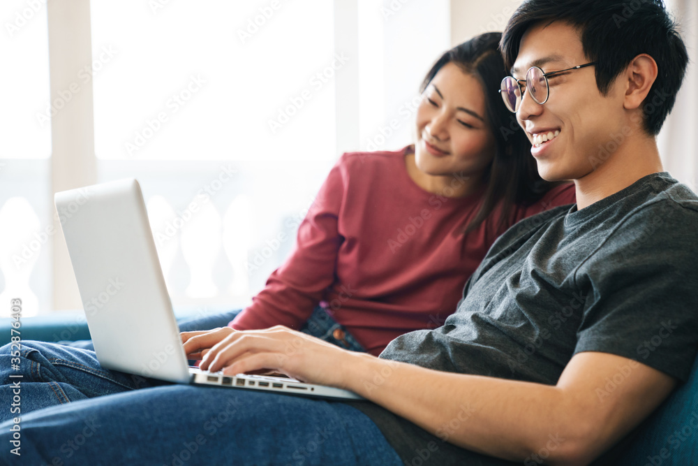 Photo of asian couple laughing and using laptop while sitting on sofa Photo of asian couple laughing and using laptop while sitting on sofa
