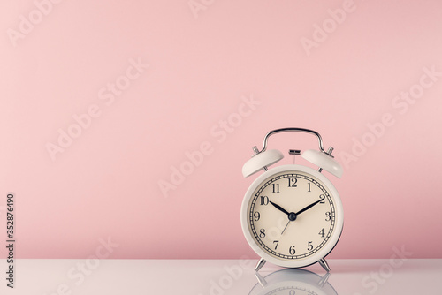  белый будильник на белом столе и розовом фоне