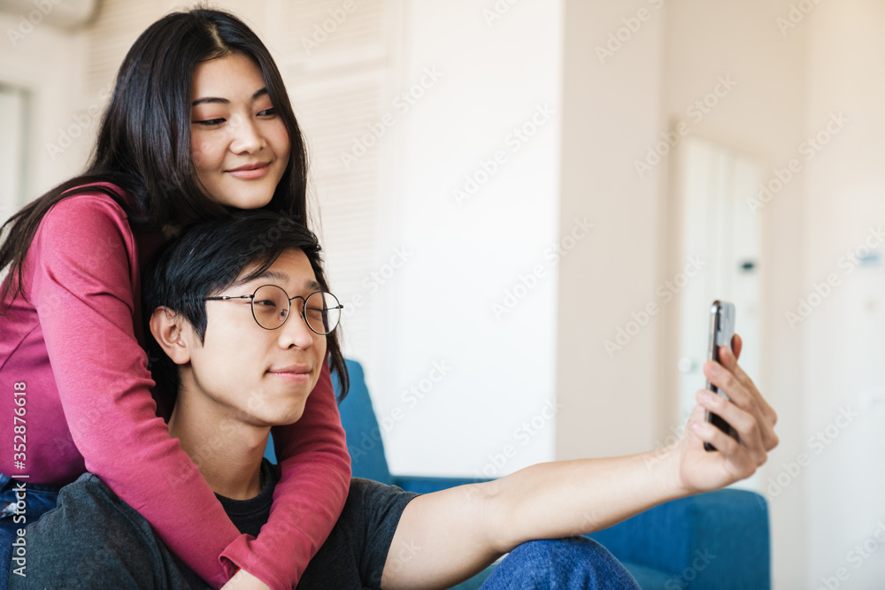 Photo of asian couple taking selfie photo on mobile phone while sitting Photo of asian couple taking selfie photo on mobile phone while sitting