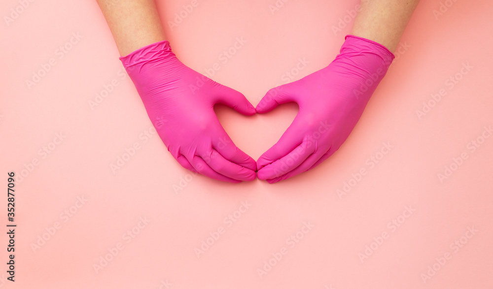 Top view, female hands in protective gloves folded together in form of a heart on pink background.
