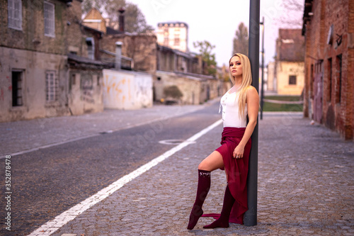 Blonde young pretty girl dancer perform in empty street leaning on pole