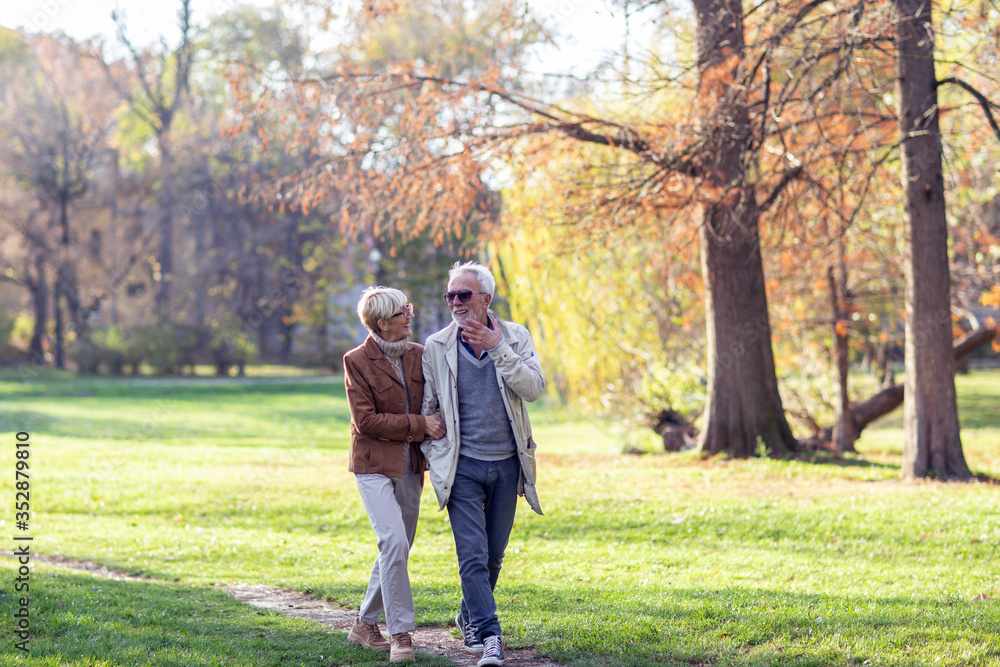 Mature couple walking thru public park on sunny day and smile