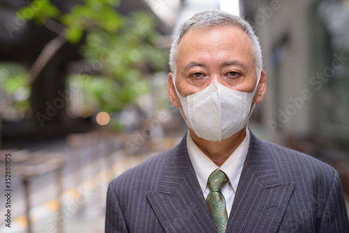 Face of mature Japanese businessman with mask in the city