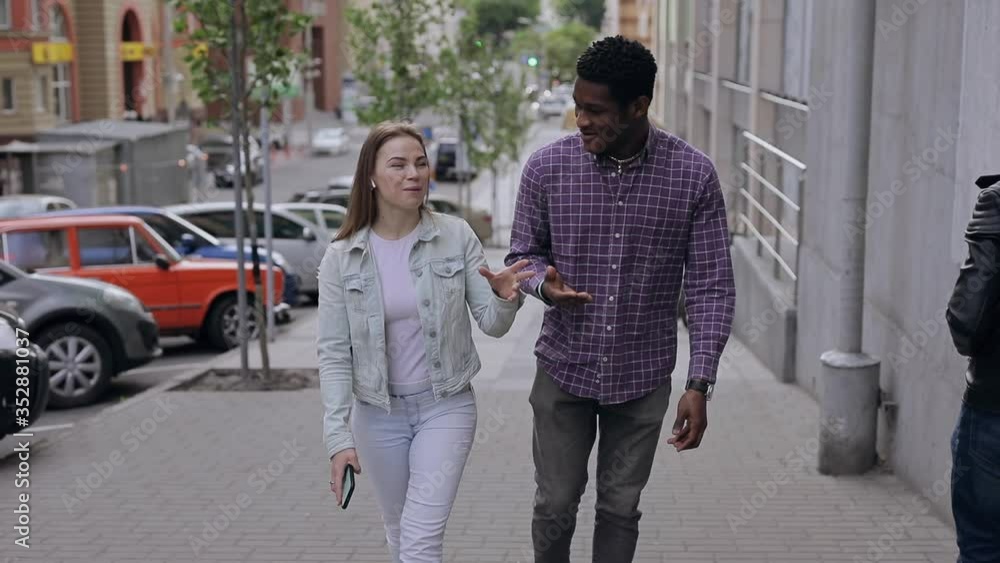 Two multiracial friends walking and talking in a city street Two multiracial friends walking and talking in a city street