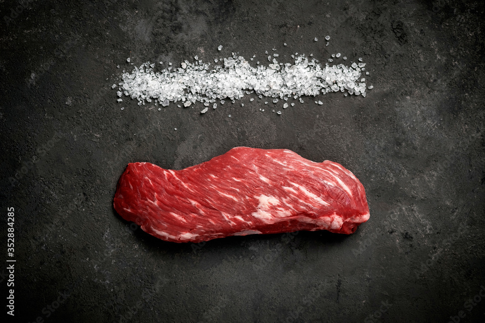 Raw beef tenderloin or bavet steak with salt on a dark stone background