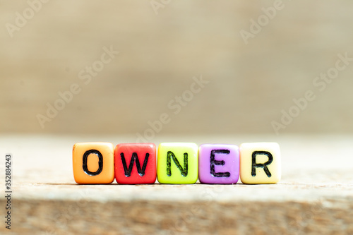 Colorful bead with black letter in word owner on wood background photo