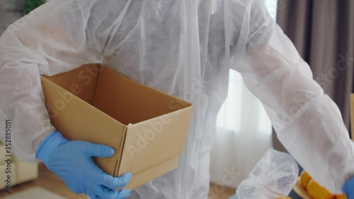 Close up of volunteer packing food in box for delivery wearing protective suit during gloabal covid-19 pandemic photo