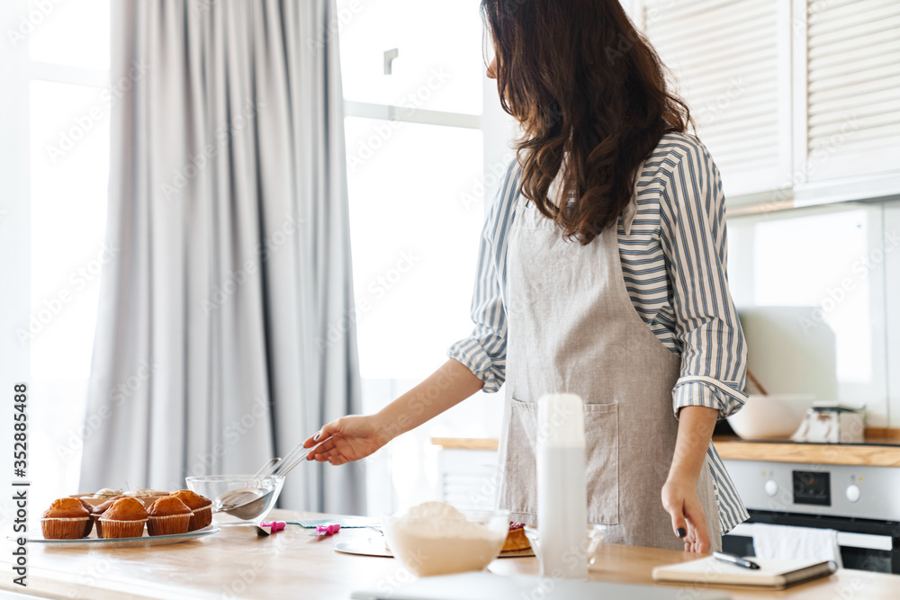 Image of focused brunette woman wearing apron cooking pie with recipe Image of focused brunette woman wearing apron cooking pie with recipe