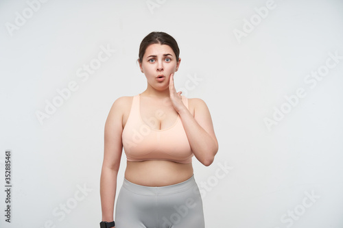 Obraz na plátně Bewildered young dark haired chubby woman with ponytail hairstyle holding raised