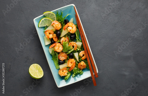 Salad with shrimp, pineapple and fresh herbs in a blue plate on a black background. Healthy food. Top view.
