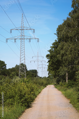 transmission line or overhead power cable with electricity pylons along rural dirt track country lane path through german countryside