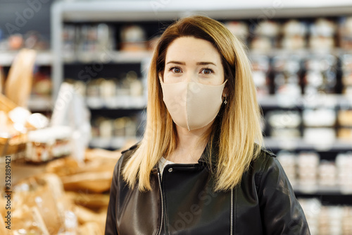 Portrait of a young pretty woman in a protective medical mask who is shopping at the supermarket during a pandemic. The buyer makes purchases at the grocery store. photo