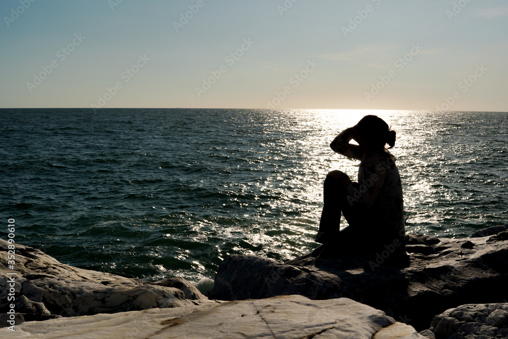 A woman silhouette watching sun on the beach at sunset