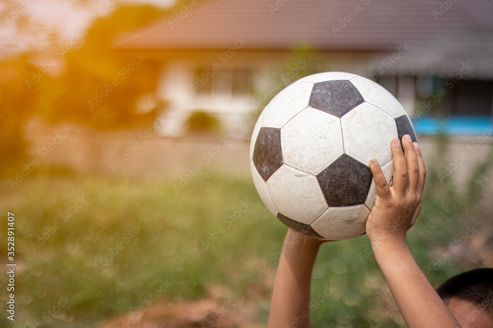 Asian boy holding old soccer ball at the countryside in the morning with sunlight effect.