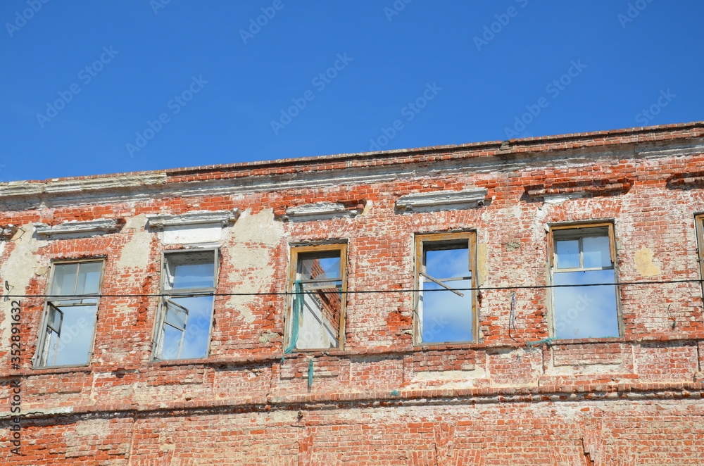 Brick facade of an abandoned old building with windows.