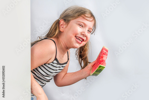 Happy little child with watermelon. Smiling kid girl eating watermelon slice  against white wall background  Copy space