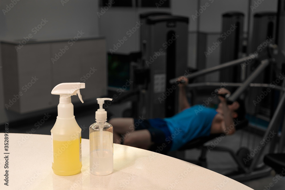 Close up spray bottle of yellow disinfectant and alcohol gel with blurred background of Asian man workout in gym. Concept for prevention and protection of Corona virus Covid 19 in fitness center. Close up spray bottle of yellow disinfectant and alcohol gel with blurred background of Asian man workout in gym. Concept for prevention and protection of Corona virus Covid 19 in fitness center.