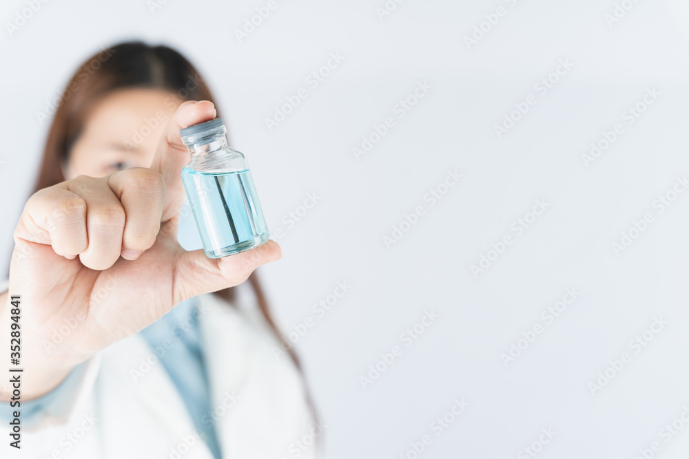 Closeup hand of woman doctor or scientist wearing medical mask and holding medicine liquid vaccine vial bottle. COVID 19 or coronavirus concept.