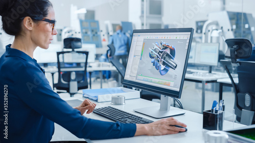 Industrial female Engineer Working on a Personal Computer, Screen Shows CAD Software with 3D Prototype of Engine. Busy Factory with Professional Workers High-Tech Machinery