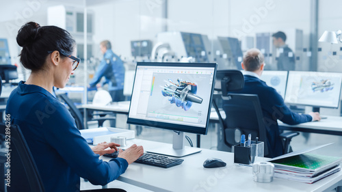 Industrial female Engineer Working on a Personal Computer, Screen Shows CAD Software with 3D Prototype of Electric Engine. In Background Modern Factory with High-Tech CNC Machinery