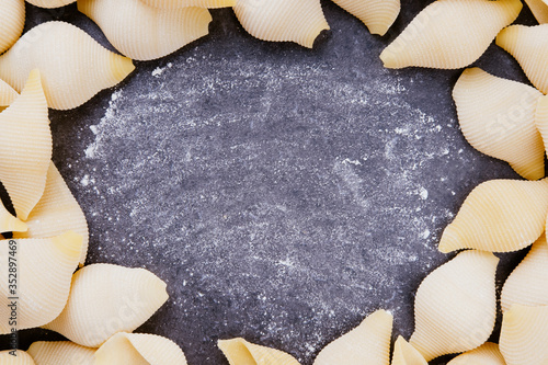 Raw conchiglie rigate pasta and flower on grey stone table. Frame with space for text. Studio top view shot flat lay