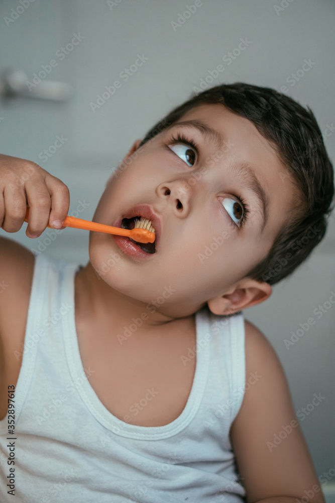 cute kid looking up while brushing teeth in bathroom cute kid looking up while brushing teeth in bathroom