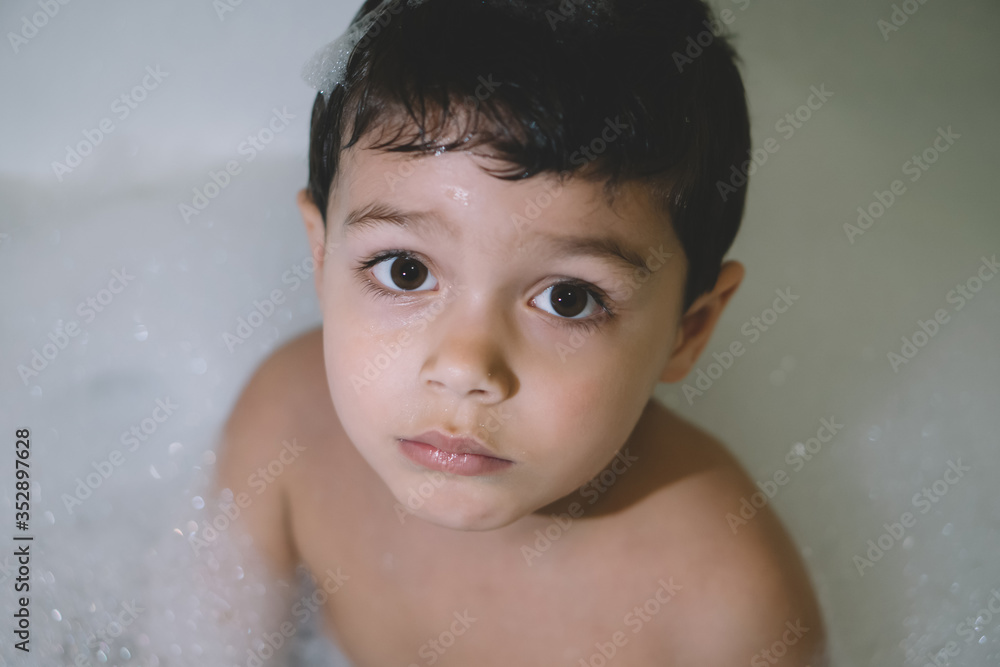 overhead view of adorable boy looking at camera while taking bath overhead view of adorable boy looking at camera while taking bath