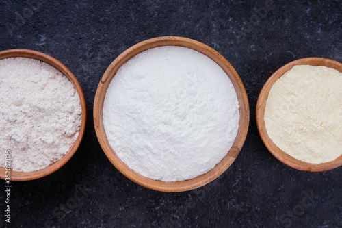 Rice flour, corn flour and whole grain flour in wooden bowls on dark background. Flat lay top view, studio shot