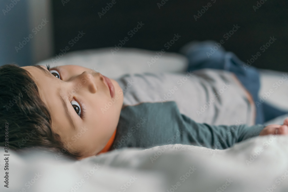 selective focus of thoughtful boy lying on bed at home and looking away selective focus of thoughtful boy lying on bed at home and looking away