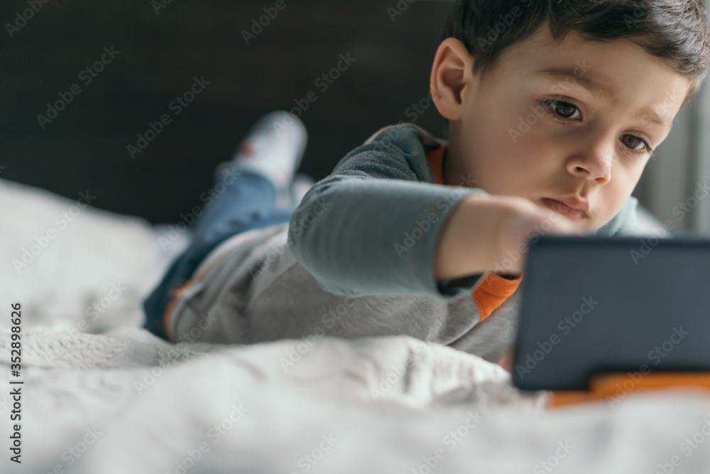 selective focus of cute boy touching smartphone while lying in bed selective focus of cute boy touching smartphone while lying in bed