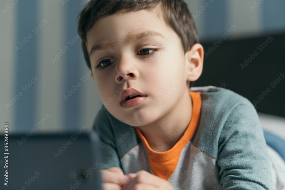 selective focus of concentrated boy looking online lesson on smartphone in bed selective focus of concentrated boy looking online lesson on smartphone in bed