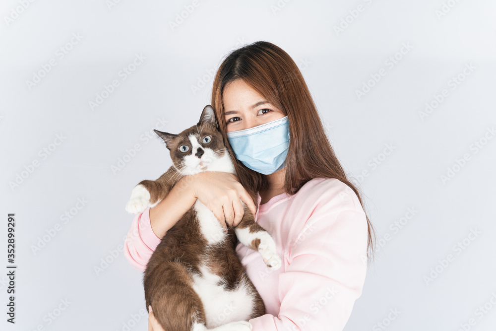 Asian beautiful happy woman wearing a medical protection face mask for protect the coronavirus, filter dust PM 2.5, cold and allergic to cat fur and she carry a cat on the white background Asian beautiful happy woman wearing a medical protection face mask for protect the coronavirus, filter dust PM 2.5, cold and allergic to cat fur and she carry a cat on the white background